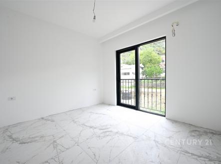 Světlý pokoj s velkými okny a balkónovými dveřmi, moderní dlažba, bílé stěny, výhled do zahrady, novostavba