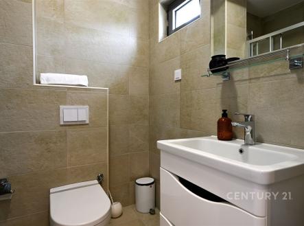 Koupelna s moderními dlaždicemi, elegantní umyvadlo a zrcadlo. Kompaktní prostor s úložnými možnostmi, čisté linie a světlé barvy.
