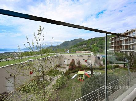 Balkón s proskleným zábradlím nabízí výhled na hory a mořem, moderní architektura budov s terasovým designem, ideální pro relaxaci.