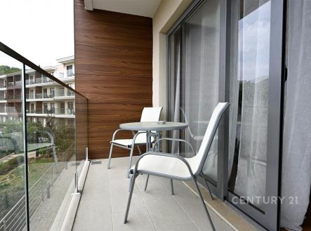 Balkon s moderními skleněnými zábradlími, dlažbou a výhledem do zeleně, ideální pro relaxaci a venkovní posezení.