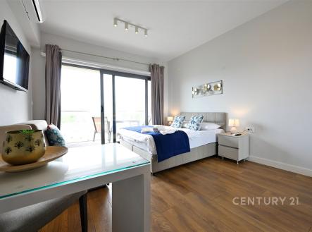 Světlá ložnice s parketovou podlahou, velkými okny a moderním dekorem, nabízí útulné a stylové prostředí vhodné pro relaxaci.
