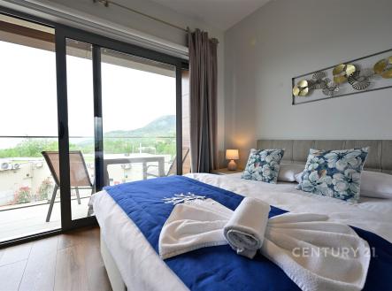 Prostorná ložnice s parketovou podlahou a velkými okny, moderní interiér, přístup na soukromý balkon s výhledem na krajinu.