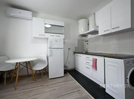 Moderní kuchyň s bílými skříňkami, dlažbou na podlaze a vestavěnými spotřebiči, světlé stěny a umělé osvětlení dodávají prostoru čistý vzhled.