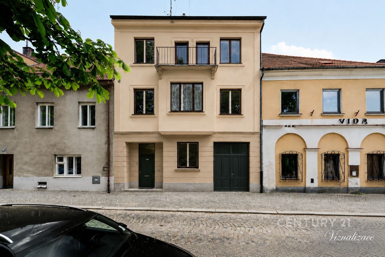 Fasáda rekonstruovaného třípatrového domu s velkými okny a balkónem, situovaný na dlážděné ulici.