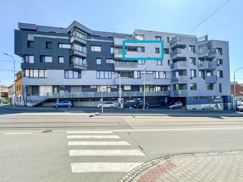 Moderní bytový dům s balkonem, fasáda v šedých tónech, velká okna, výborný stav budovy, nachází se v klidné městské lokalitě.