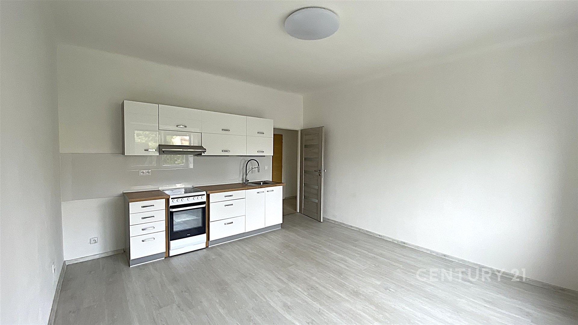 Moderní kuchyň s bílými skříňkami, vestavěnou troubou a laminátovou podlahou, světlý interiér, jednoduchý design