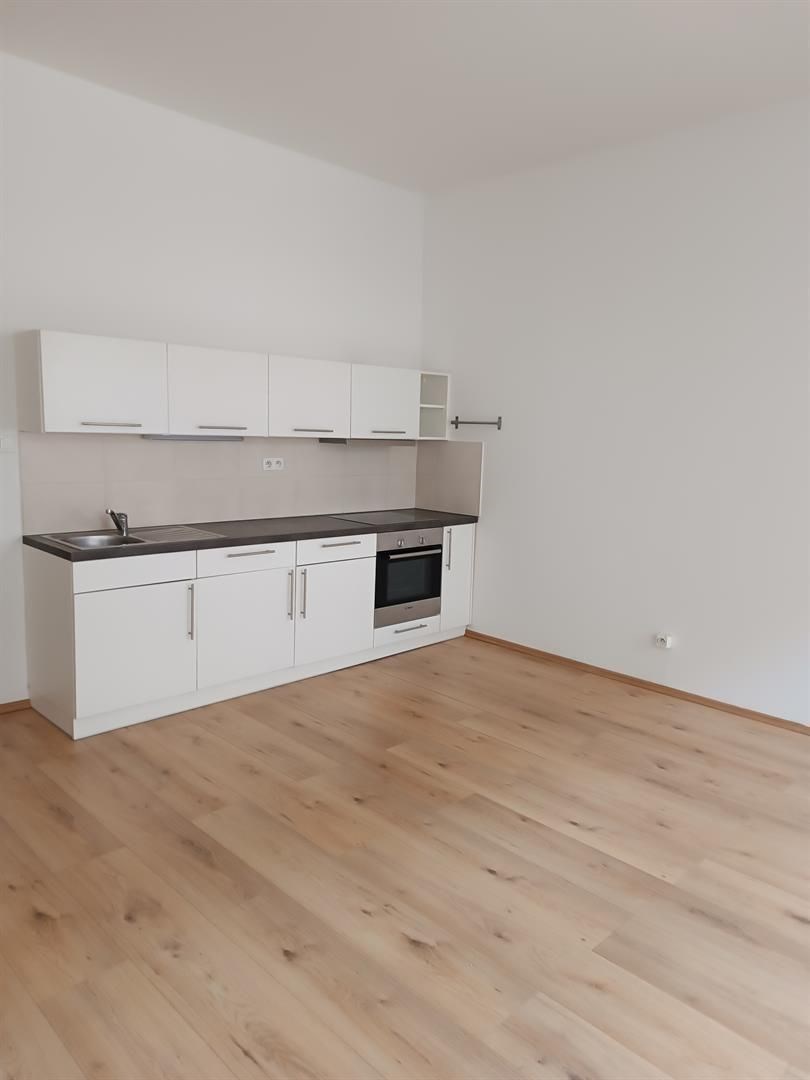 Moderní kuchyň s bílými skříňkami, parketová podlaha, světlý prostor, vestavěná trouba, minimalistický design