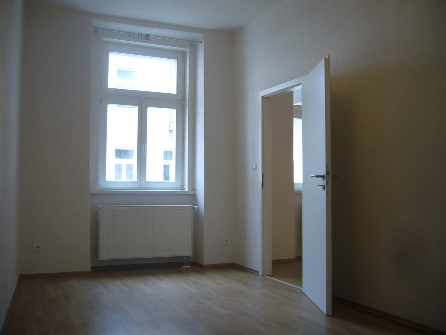Světlý obývací pokoj s parketovou podlahou a velkým oknem, nabízí moderní dispozici v rekonstruovaném bytě.