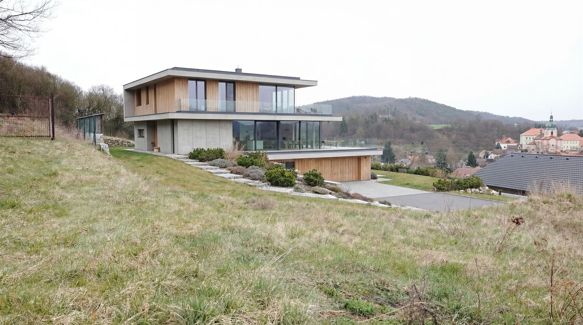 Moderní vila s dřevěným obkladem a velkými okny nabízí panoramatický výhled na okolní krajinu a zahradu, moderní architektura