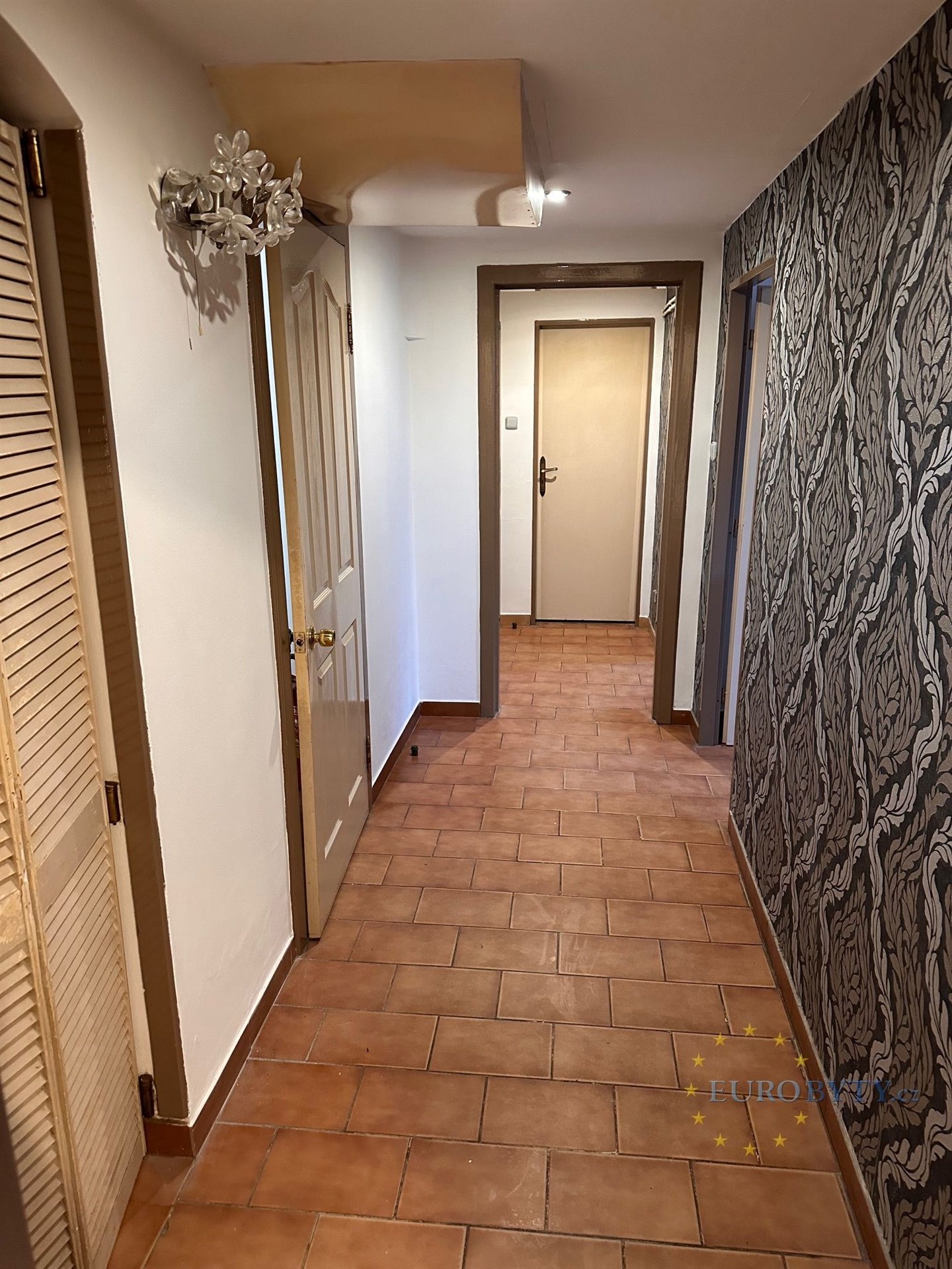 Chodba s dlažbou, stylovou tapetou a několika dveřmi v rekonstruovaném bytě.