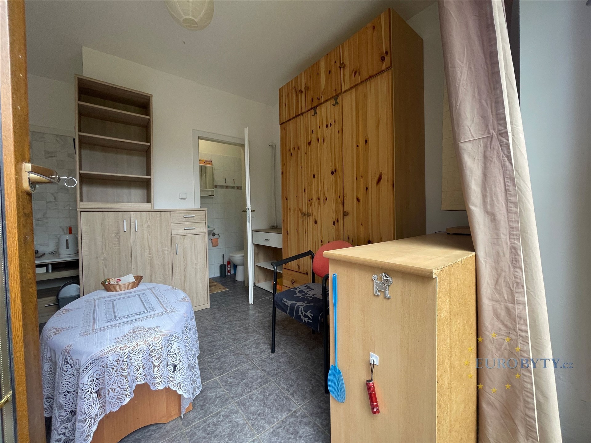 Jednolůžkový pokoj s dlažbou, vestavěné skříně z dřeva, světlý interiér s přístupem do koupelny, rustikální styl nábytku.