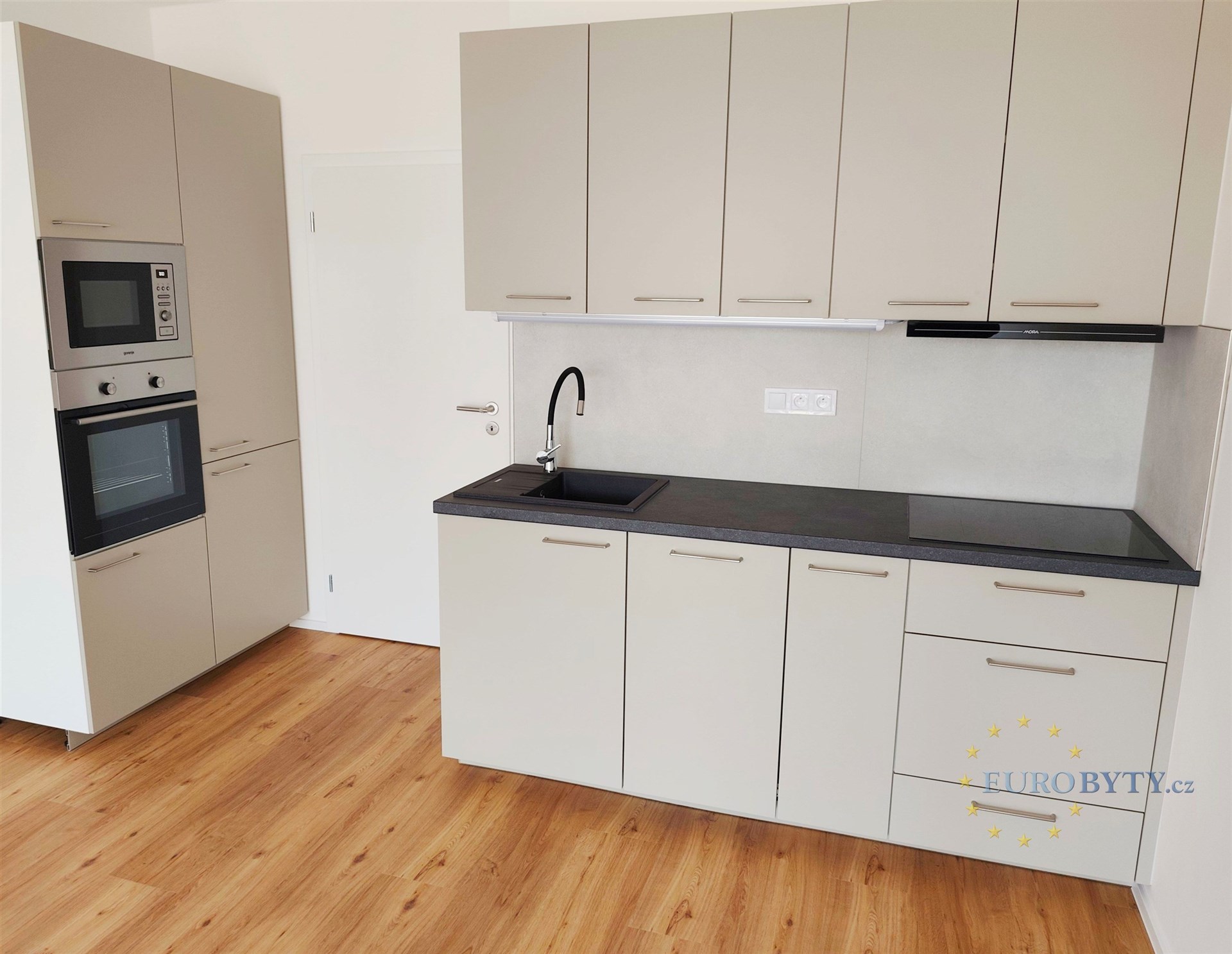 Moderní kuchyň s parketovou podlahou, vestavěné spotřebiče a světlé skříňky, elegantní pracovní deska a prostor pro přípravu jídel