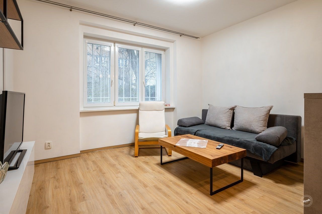 Světlý obývací pokoj s parketovou podlahou, velkými okny a moderním nábytkem, ideální pro útulné bydlení v rekonstruovaném bytě.