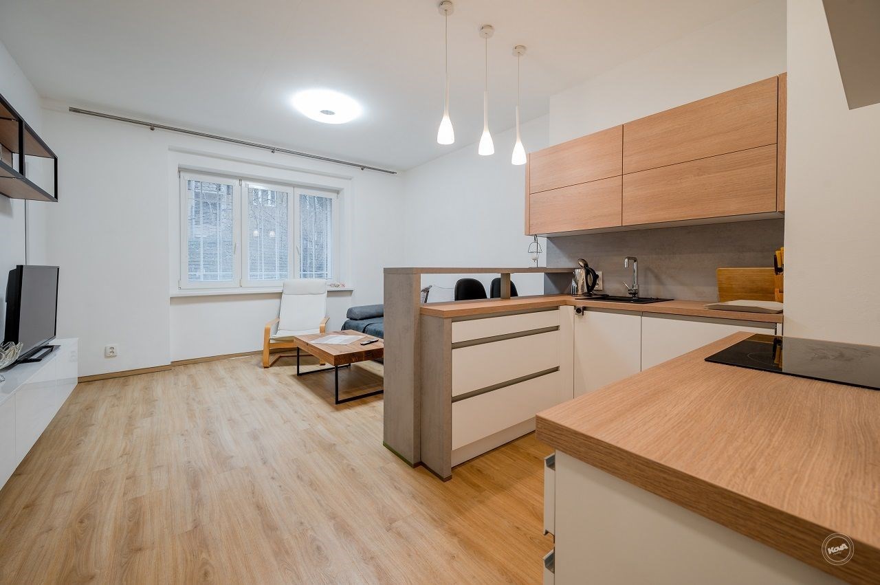 Moderní kuchyň s dřevěnou pracovní deskou, parketová podlaha, propojena s obývacím pokojem, světlý prostor díky velkým oknům.