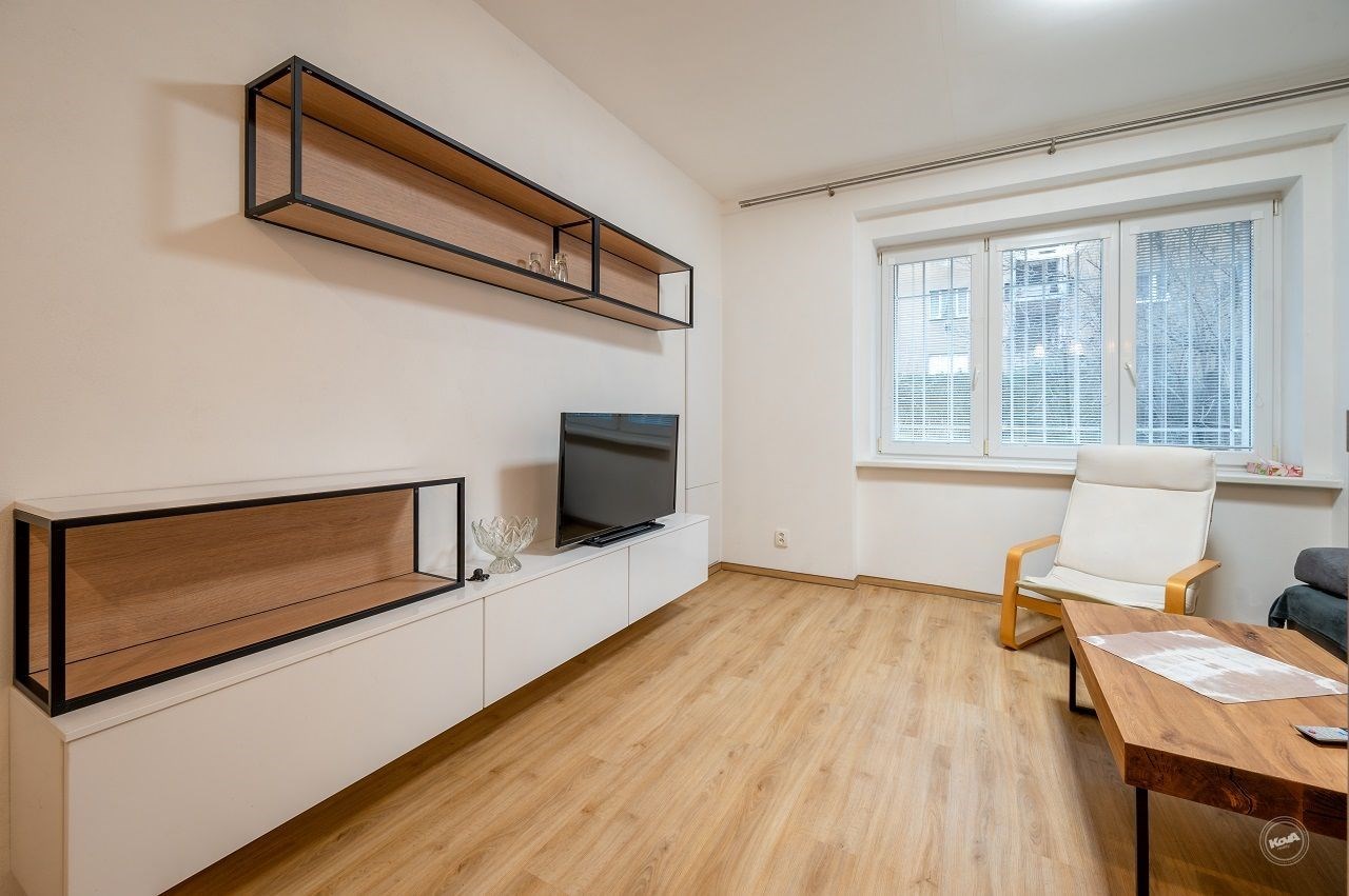 Světlý obývací pokoj s parketovou podlahou, moderním nábytkem a velkými okny, které zajišťují dostatek přirozeného světla.