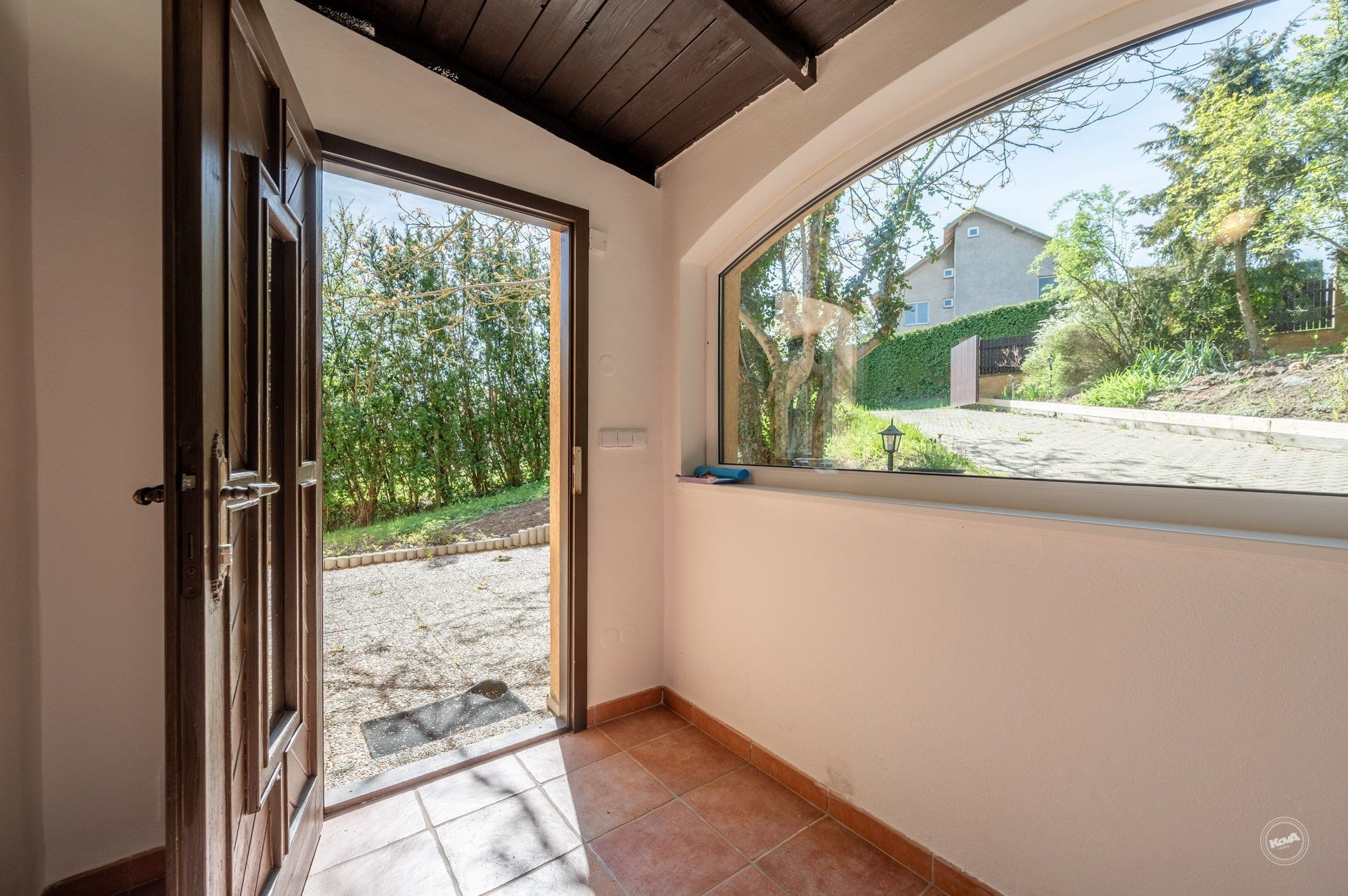 Vstupní chodba s dlažbou, velkým oknem a dřevěným stropem nabízí pohled na zahradu, působí světlým a moderním dojmem.