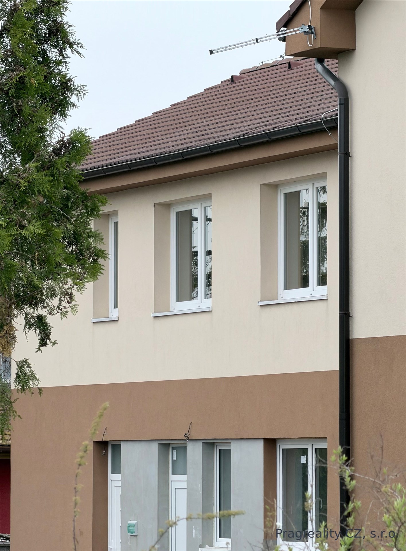 Fasáda rodinného domu s moderními okny, světlá omítka, nová střecha, klidná lokalita.