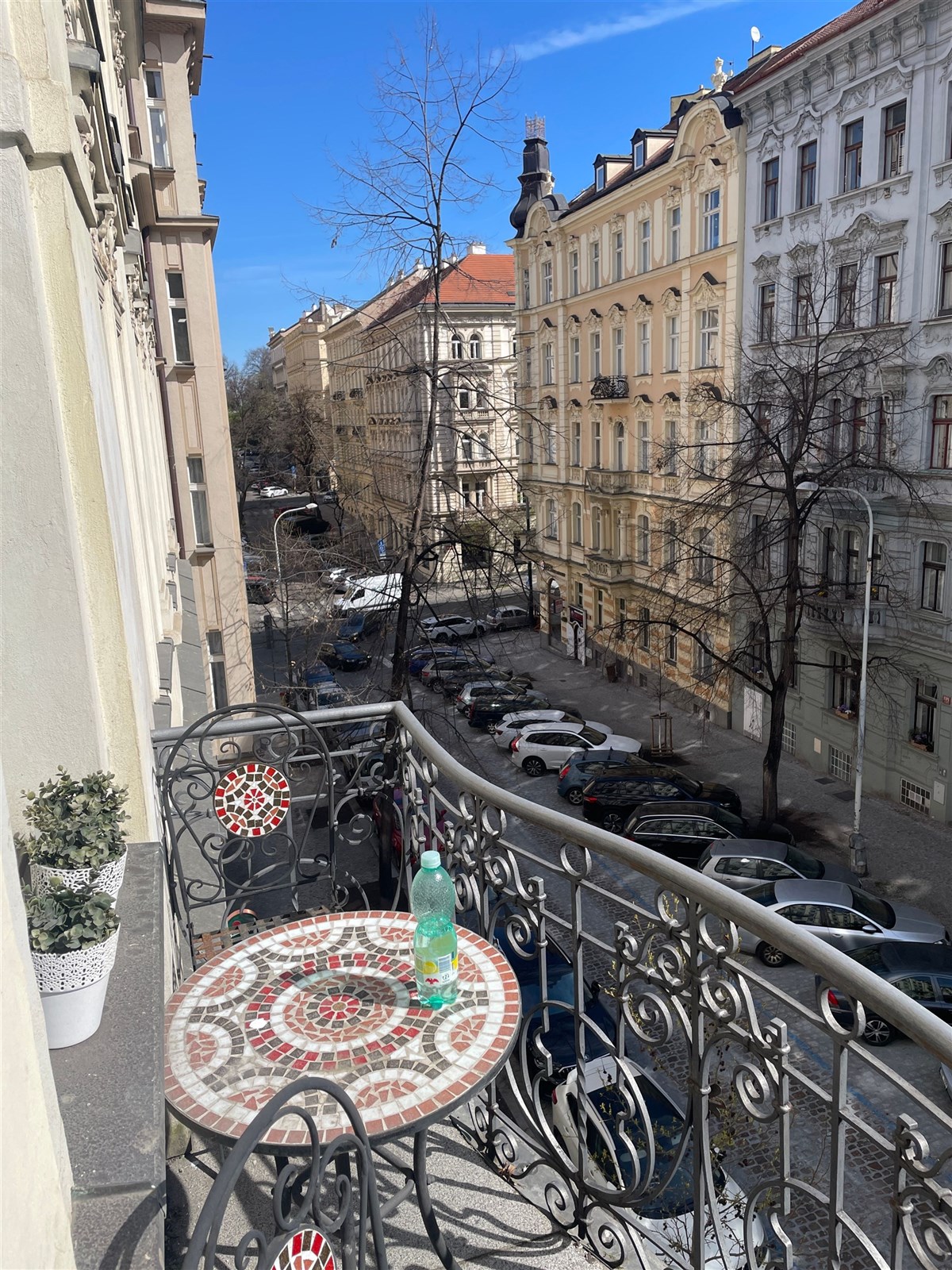Balkon s kovaným zábradlím nabízí výhled na historické budovy. Stoleček s mozaikou dodává prostoru starosvětský šarm.