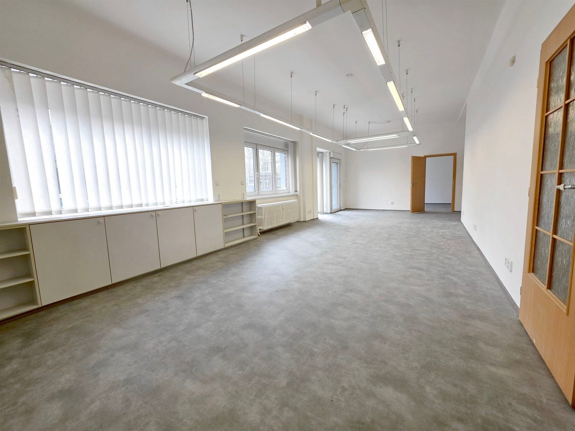 Prostorná kancelář s velkými okny, moderní podlahou z dlažby a vestavěnými skříněmi nabízí světlé pracovní prostředí.