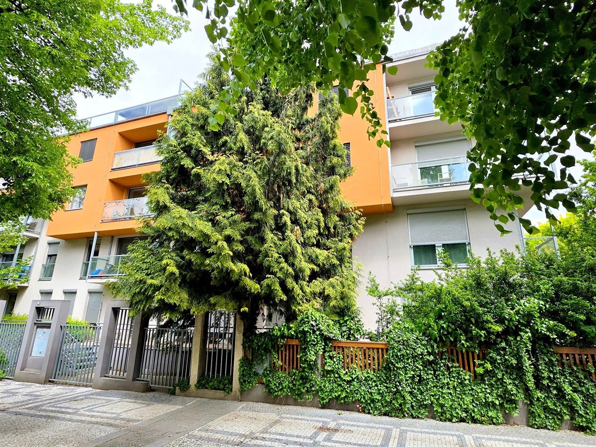 Moderní bytový dům, světlé fasády, velká okna, balkony, zelené okolí, bezpečnostní brány, klidná lokalita blízko centra