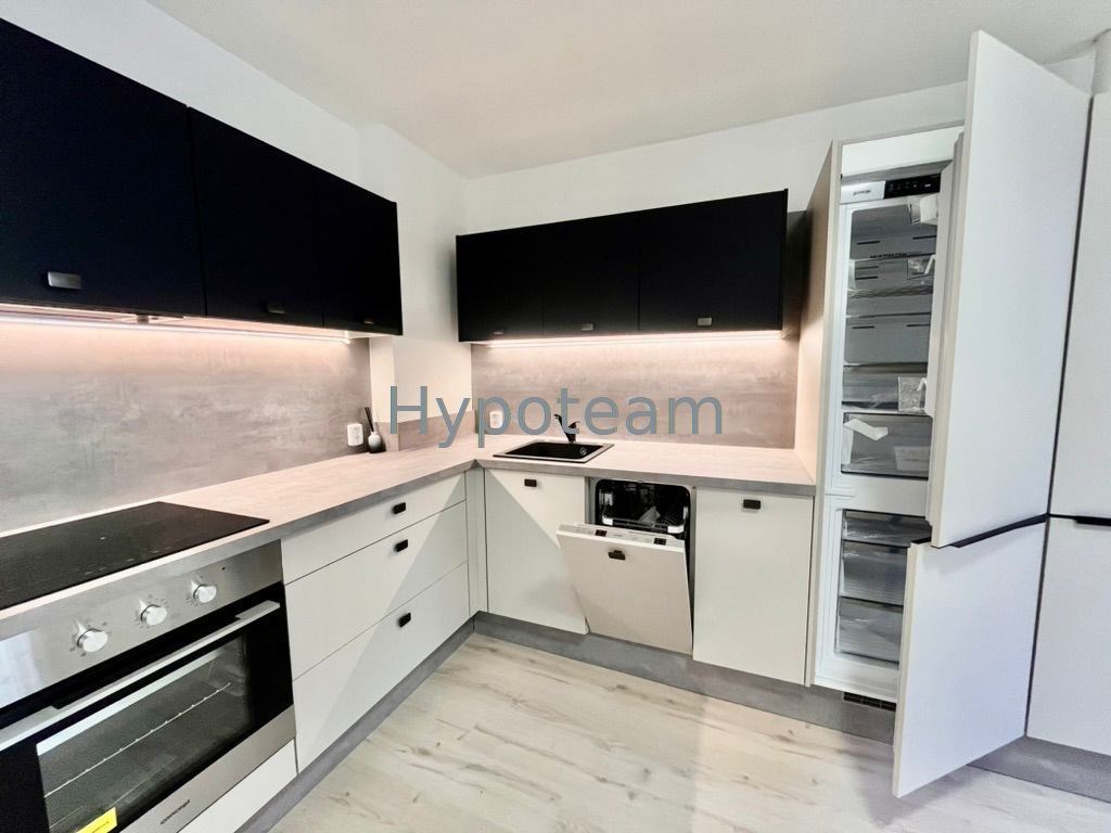 Moderní kuchyň s vestavěnými spotřebiči, světlou dřevěnou podlahou a tmavými horními skříňkami.