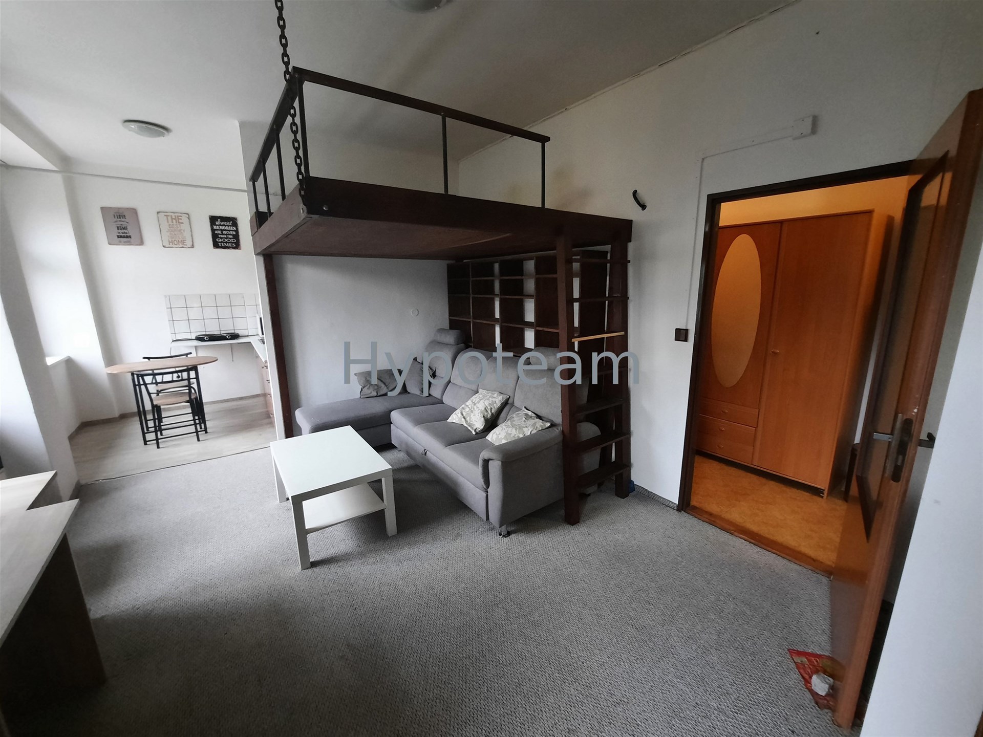 Obývací pokoj s dřevěným patrovým lůžkem, šedá sedací souprava, koberce, bílý konferenční stolek, moderní interiér, světlé pokoje.
