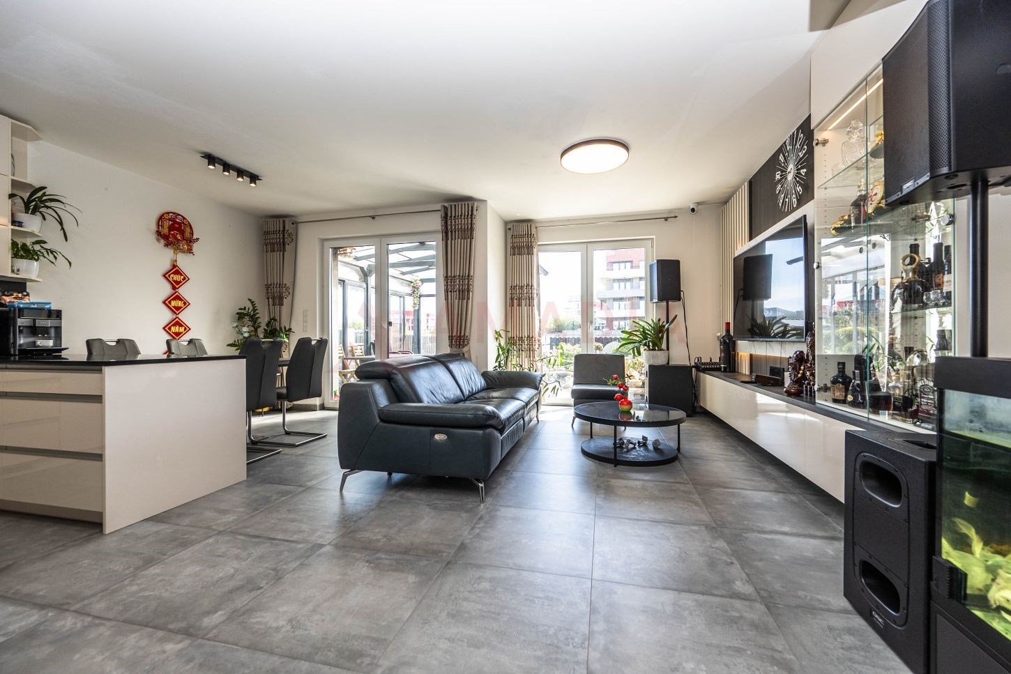 Světlý obývací pokoj s moderní dlažbou, velkými okny a elegantním nábytkem, nabízí otevřený prostor a pohodlí.