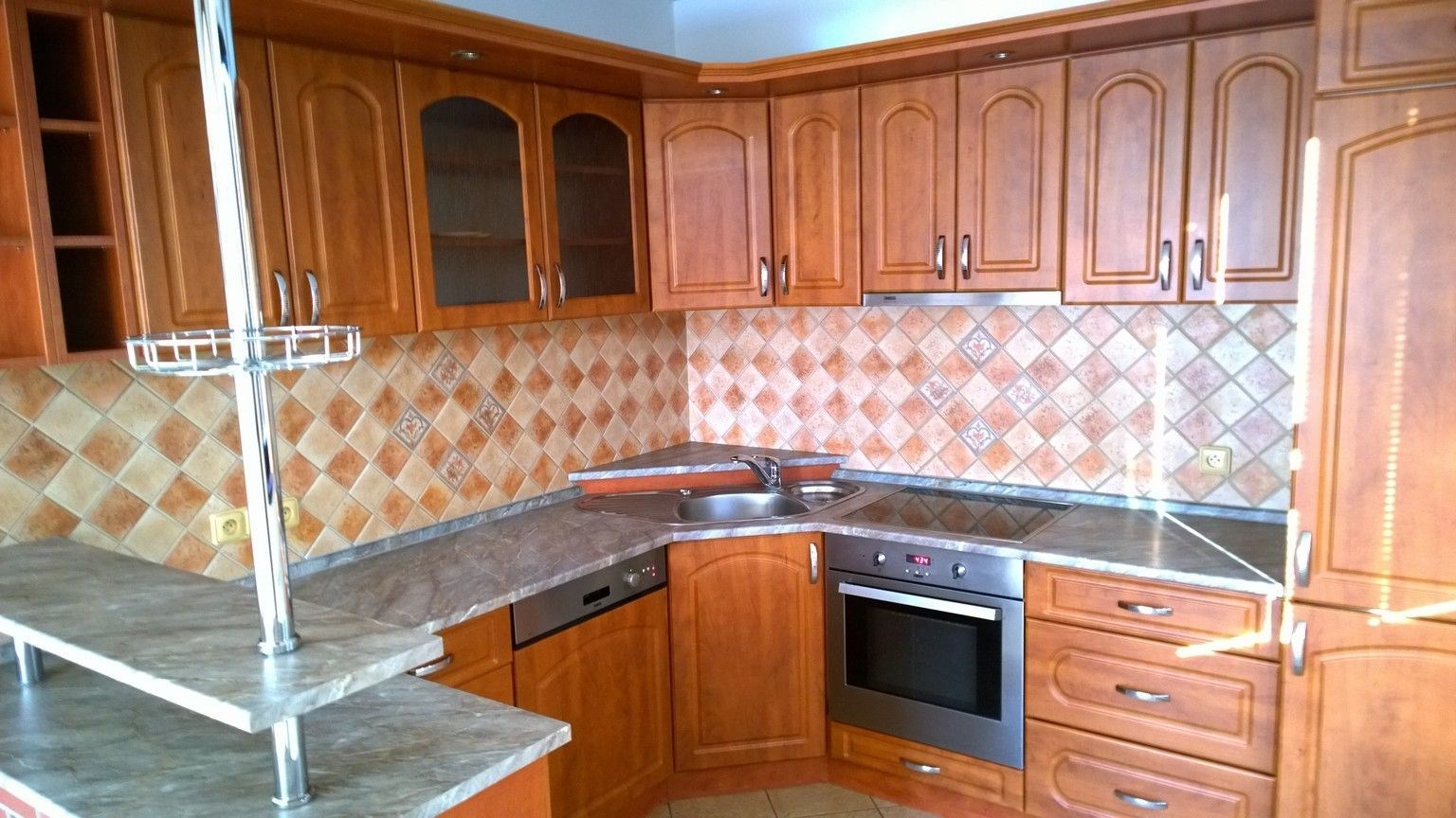 Kuchyň s dřevěnými skříňkami, moderními spotřebiči a dlažbou na stěnách, nabízí světlé prostředí a funkční prostor pro vaření.