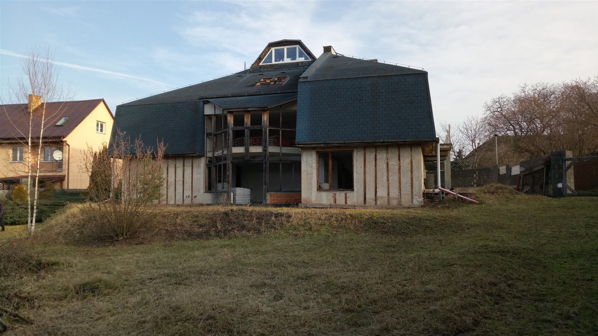 Prázdný exteriér nepodsklepeného domu s velkými okny a šindelovou střechou, potřebující rekonstrukci, zasazený v klidné oblasti.