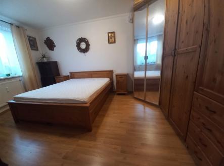 Prostorná ložnice s parketovou podlahou, vestavěnými skříněmi a světlými okny, která zajišťují moderní a komfortní prostředí.