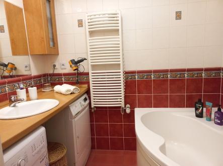 Koupelna s moderní dlažbou a bordó obklady, vybavena rohovou vanou a praktickým topným žebříkem, nabízí útulné a funkční prostředí.