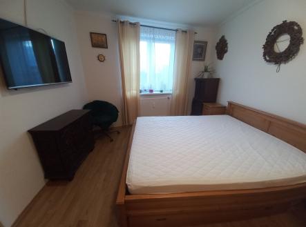 Prostorná ložnice s dřevěnou podlahou, velkou postelí a světlem z velkého okna, moderní nábytek a dekorace vytvářejí útulný interiér.