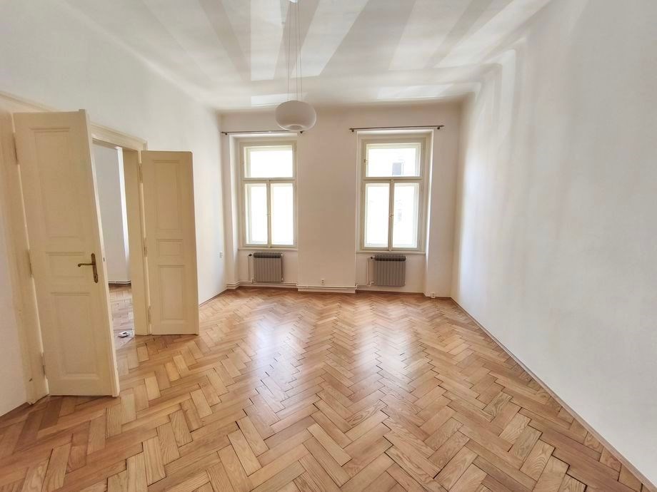 Světlý obývací pokoj s parketovou podlahou a velkými okny, který nabízí moderní prostor ideální pro komfortní bydlení