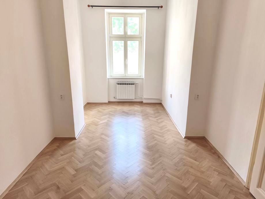 Prázdný světlý pokoj, parketová podlaha, velká okna, zrekonstruovaný prostor poskytuje moderní bydlení v klidné části města.