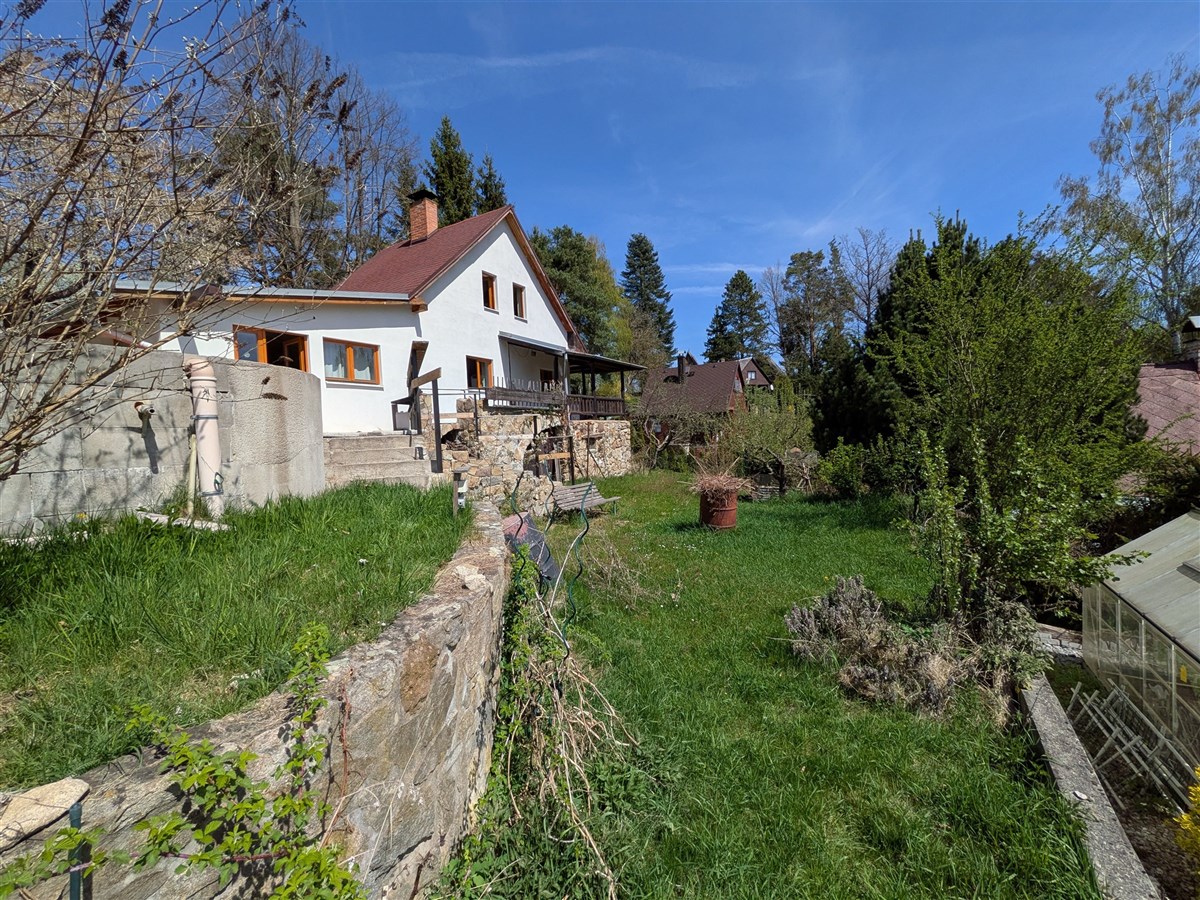 Dům se zahradou, částečně kamenný opěrný plot, velká travnatá plocha, světlá fasáda, přírodní okolí, klidná lokalita.