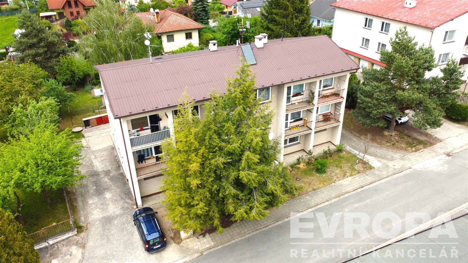 Třípatrový bytový dům s prostornými balkony, rekonstruovaná fasáda, klidná rezidenční oblast, obklopený zelení a zahradami.