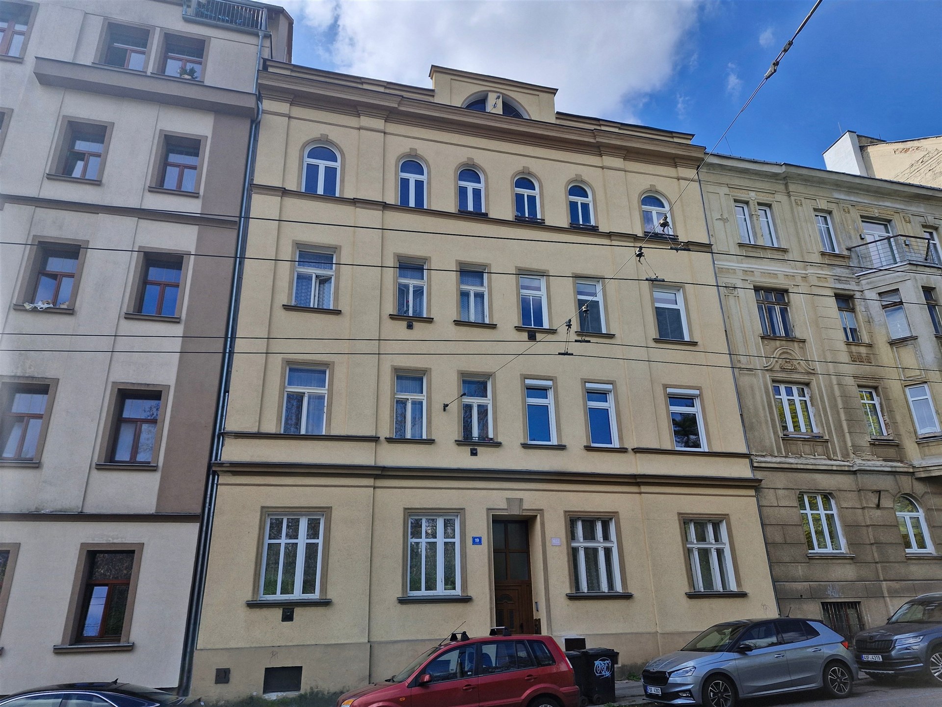 Fasáda činžovního domu s historickými prvky, velká okna, udržovaný stav, klidná lokalita městské zástavby.