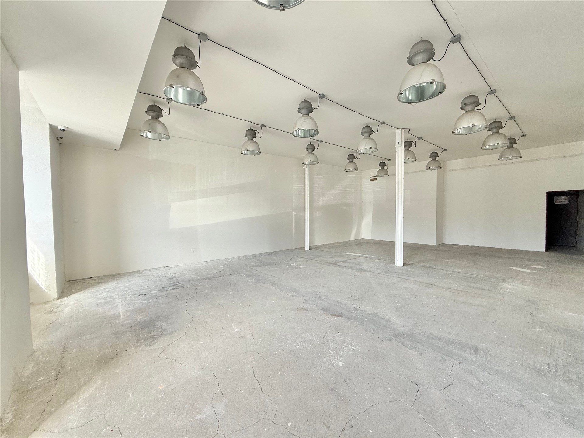Průmyslový prostor se světlými stěnami, betonovou podlahou a moderním osvětlením, ideální pro rekonstrukci nebo komerční využití.