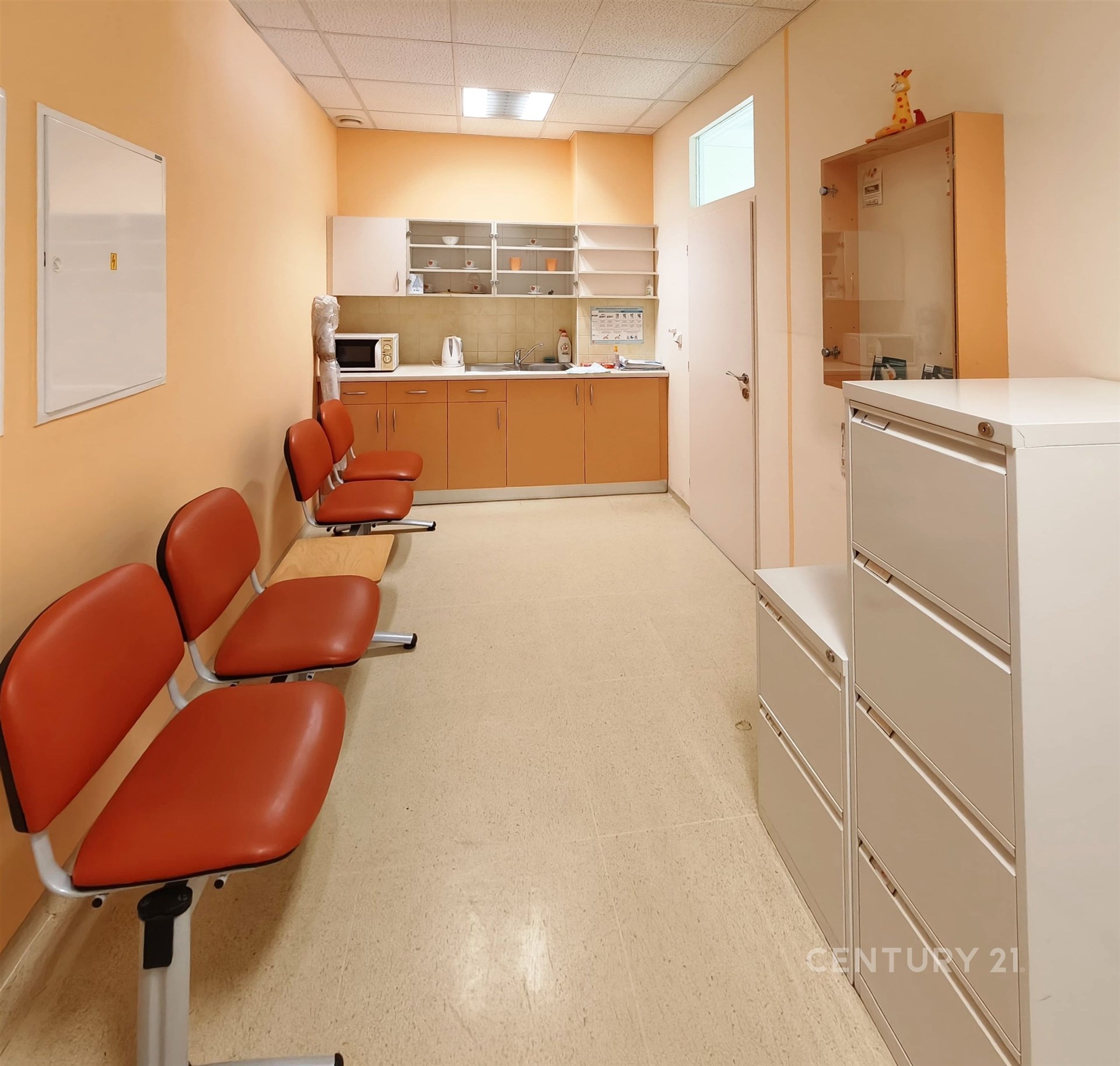 Prázdná čekárna s dlažbou, světlým nábytkem a vstupními dveřmi, vhodná pro lékařskou ordinaci nebo kancelářské prostory.