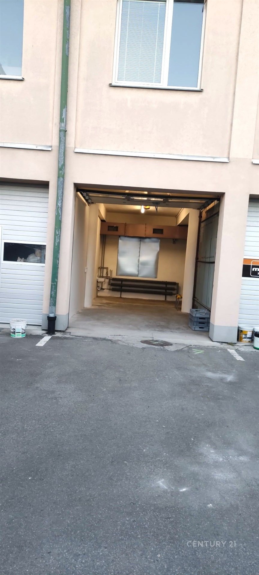 Průmyslová garáž s betonovou podlahou, vysokým stropem a rozměrnými vraty, ideální pro skladování nebo parkování větších vozidel.