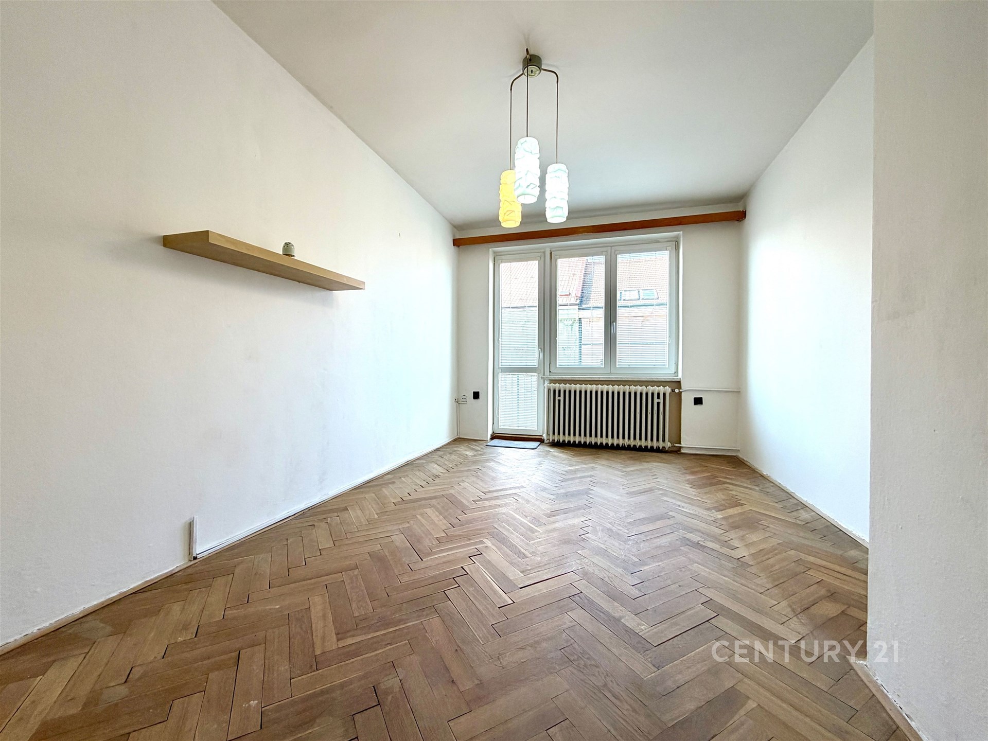 Světlý obývací pokoj s parketovou podlahou, velká okna, moderní lustr, prostor pro vestavěné skříně, příjemná atmosféra.