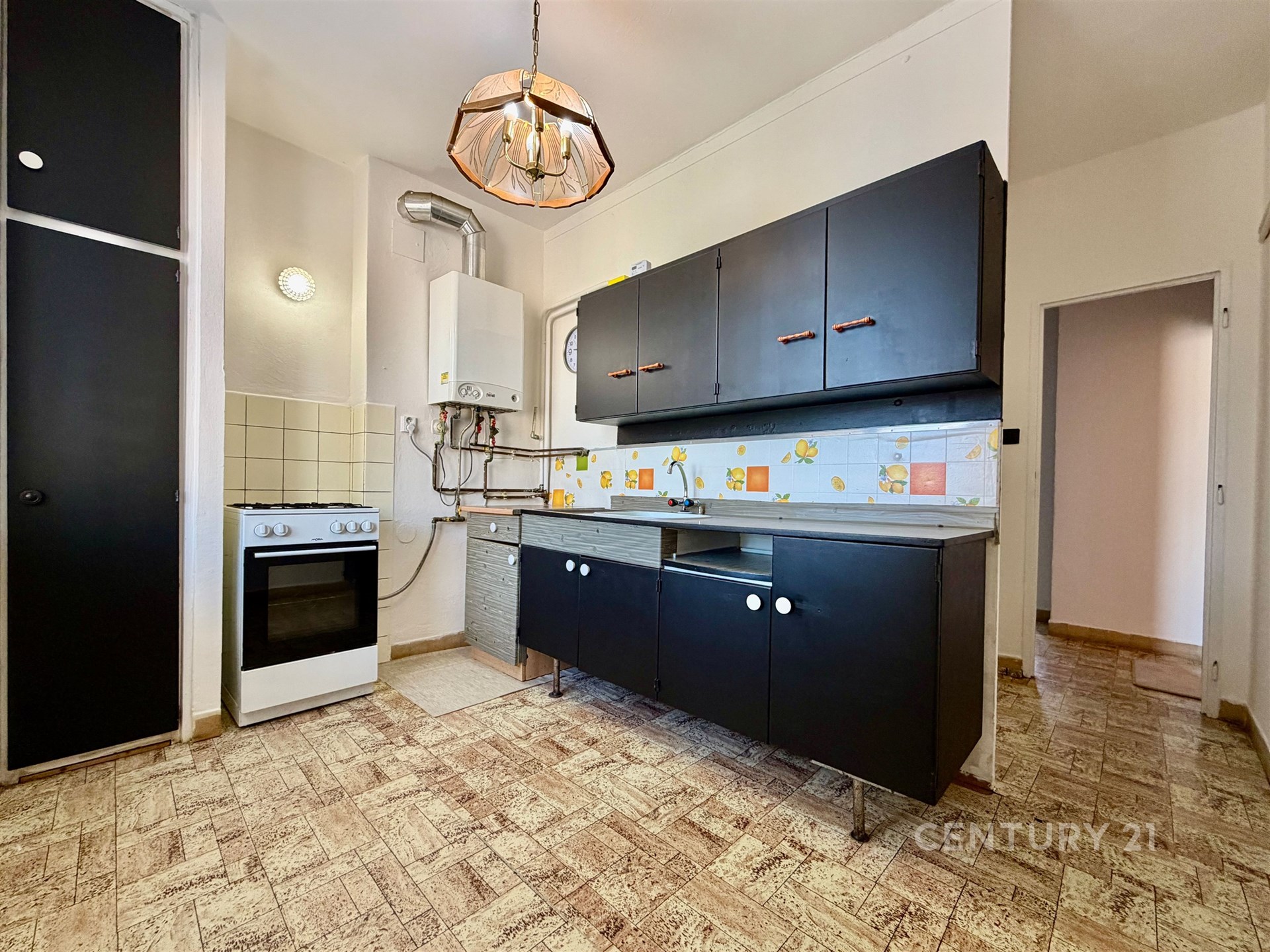 Kuchyňský prostor s retro dlažbou, černými skříňkami a plynovým sporákem, světlý interiér, vhodný k rekonstrukci.