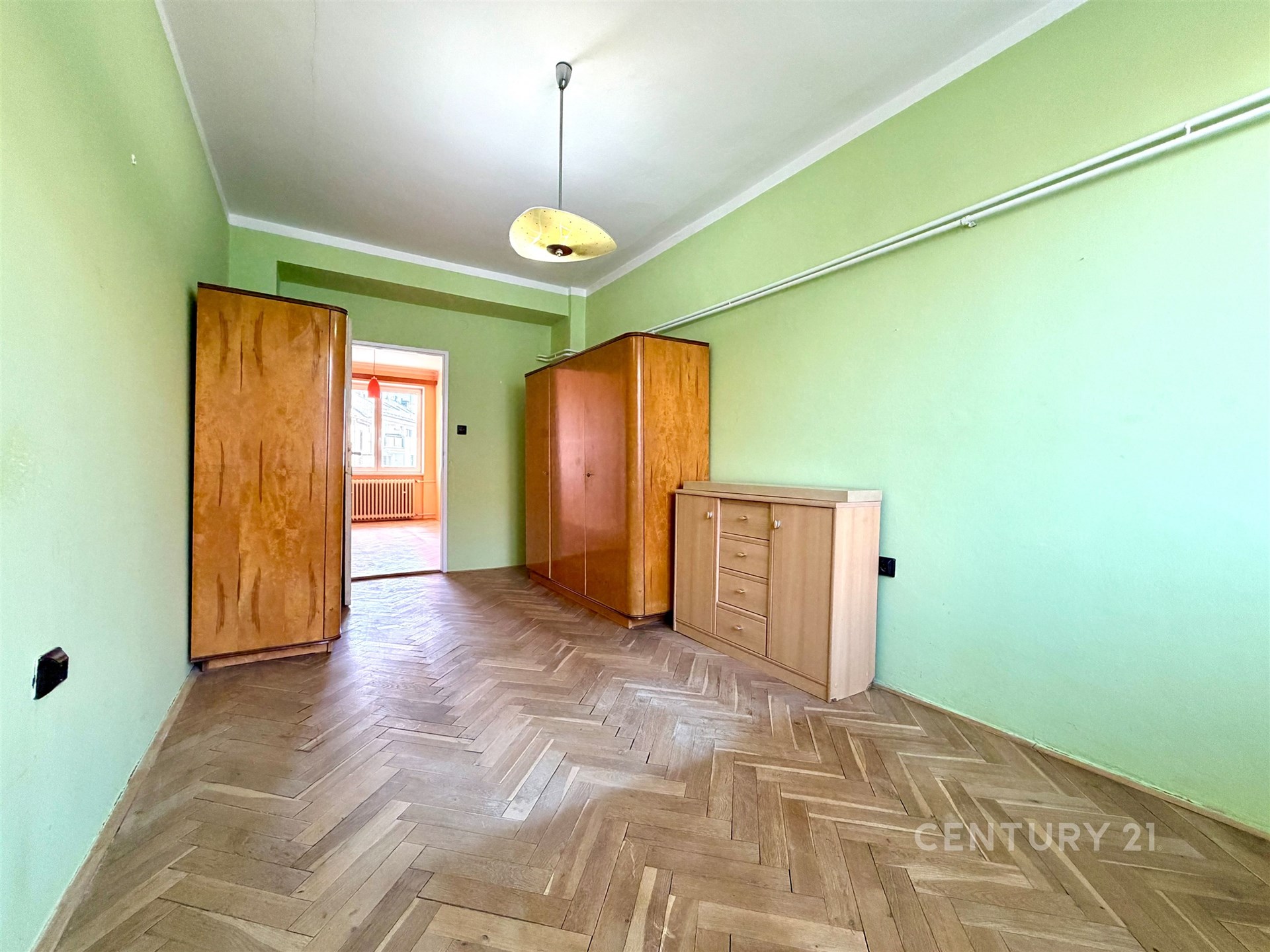 Pokoj s parketovou podlahou, zelnými stěnami a vestavěnými skříněmi, světlý interiér ideální pro moderní bydlení.