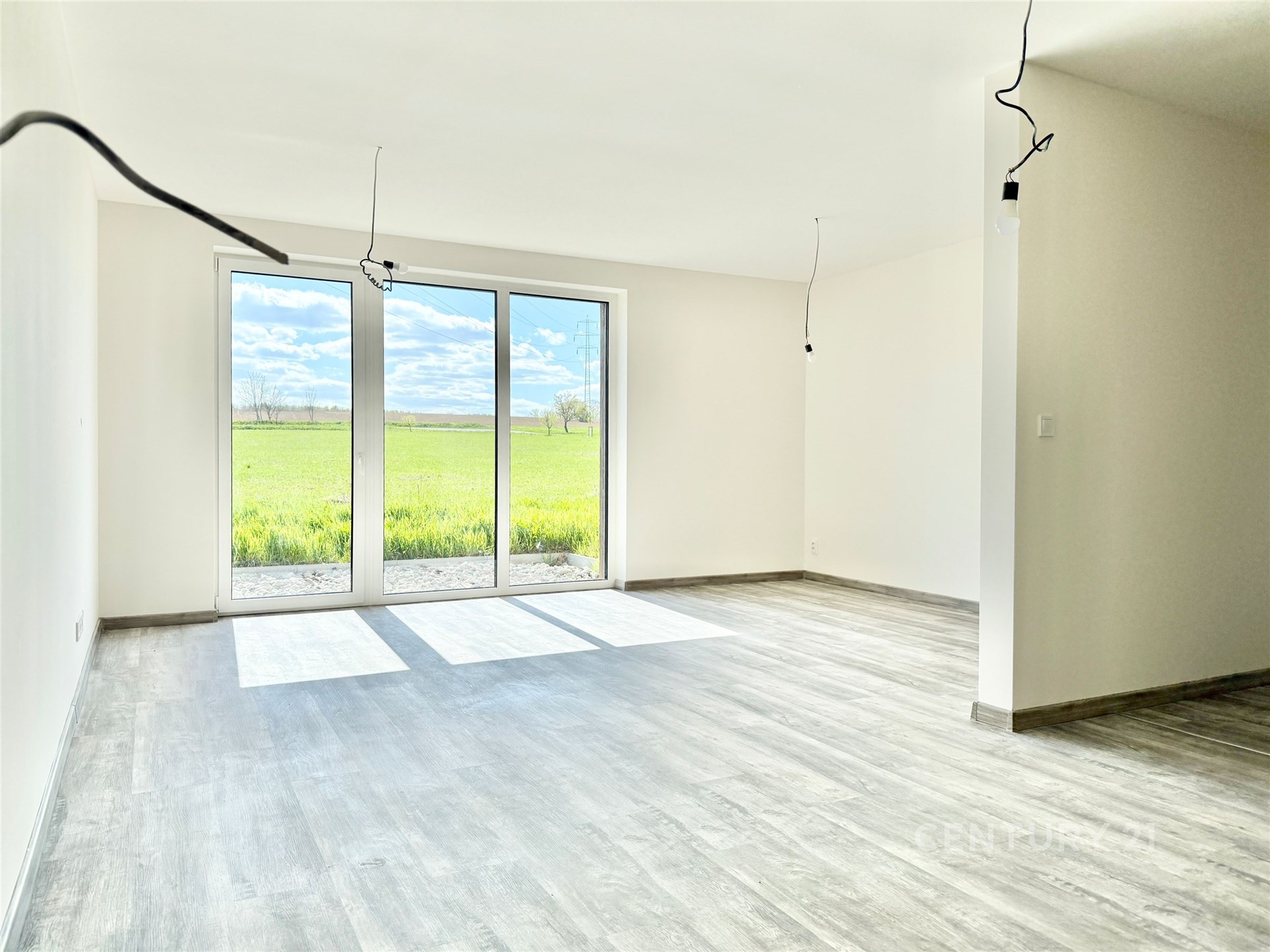 Světlý obývací pokoj s velkými okny, moderní parketová podlaha, výhled na zahradu, nově zrekonstruovaný, minimalistický styl.