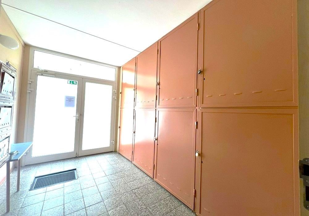 Chodba s dlažbou, vestavěné skříně a velká okna nabízí světlé prostředí. Vhodné pro moderní úložná řešení v bytovém domě.