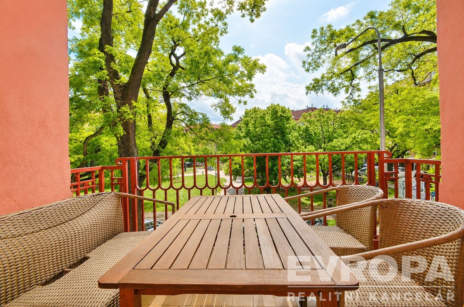 Balkon s dřevěným stolkem, výhledem na zelený park, ideální pro relaxaci. Světlé prostředí a přírodní materiály dodávají klidnou atmosféru.