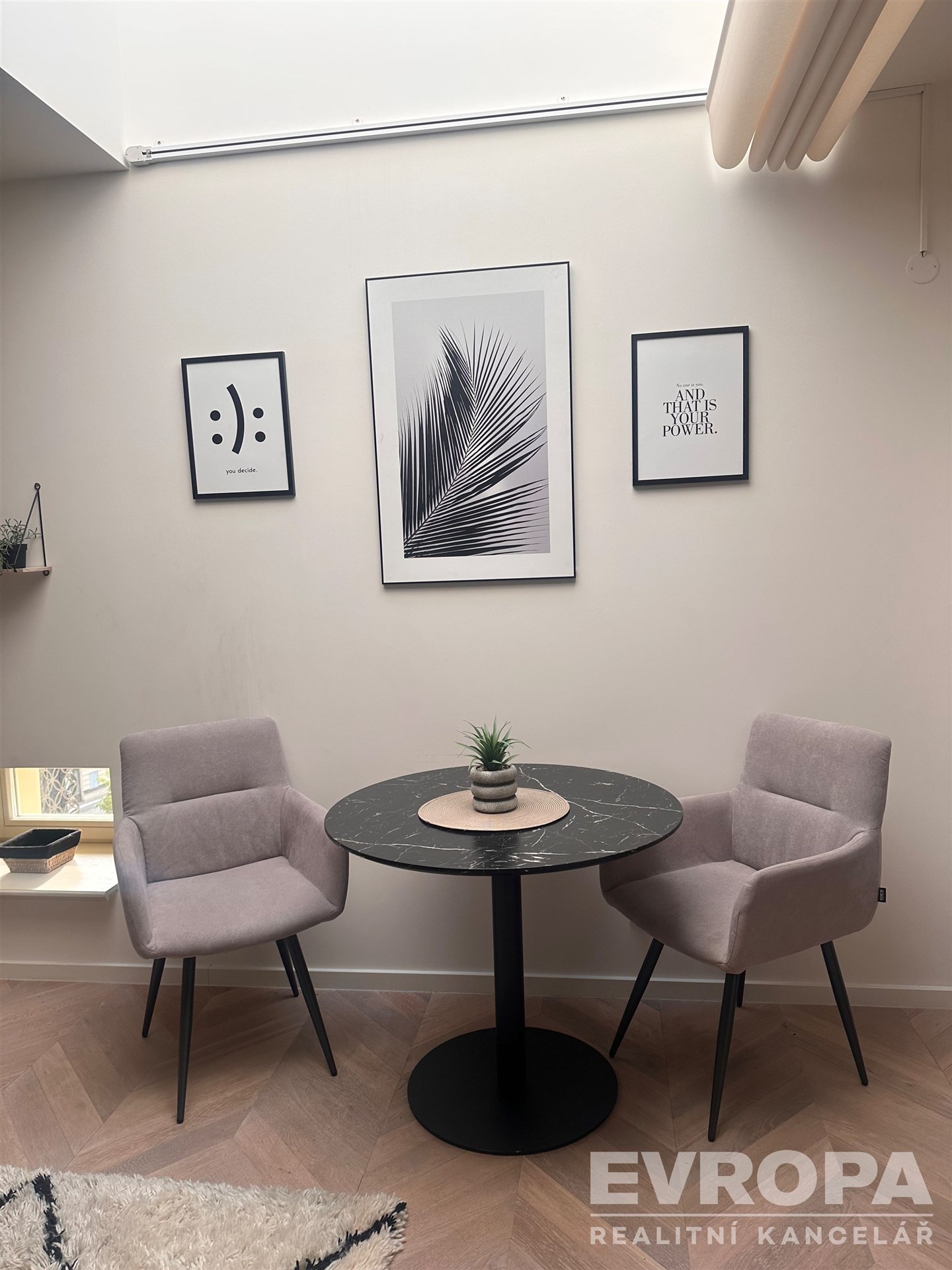 Malý jídelní kout s kulatým stolem, parketová podlaha, moderní stěny s uměním, útulný a světlý prostor.