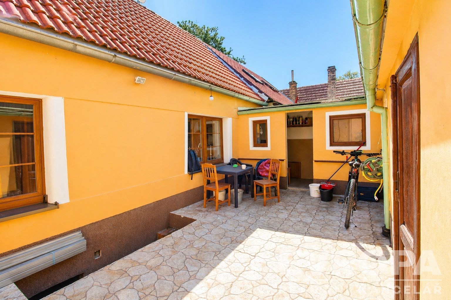 Prostorný dvorek s dlažbou, venkovním nábytkem a žlutou fasádou nabízí příjemné venkovní posezení.
