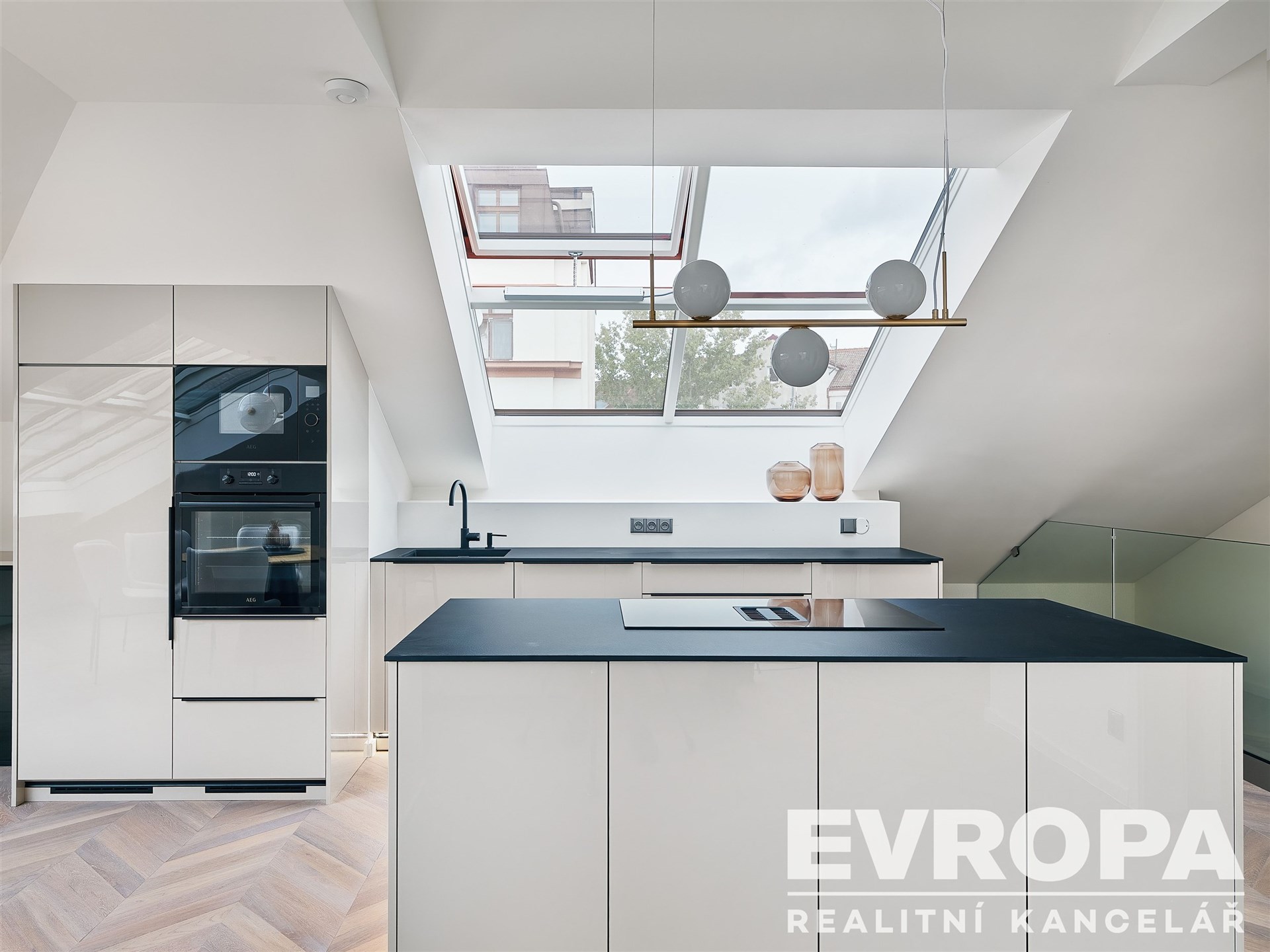 Moderní kuchyň s vestavěnými spotřebiči, parketovou podlahou a velkými střešními okny, která zajišťují světlý interiér.