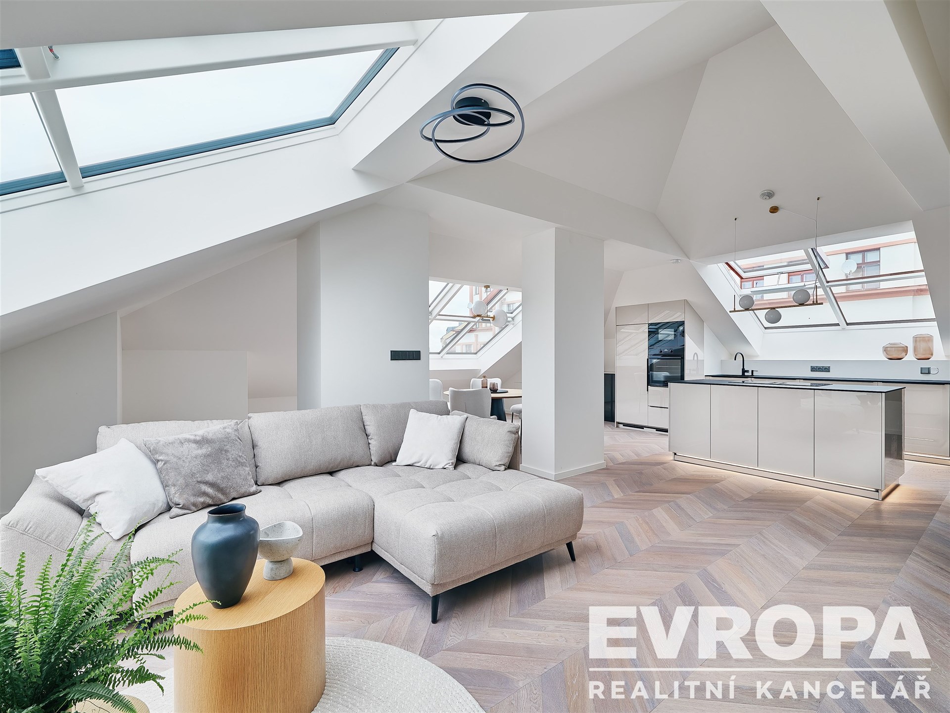 Světlý obývací pokoj s parketovou podlahou, velkými střešními okny a moderním interiérem. Propojený kuchyňský kout s ostrůvkem a designovým osvětlením